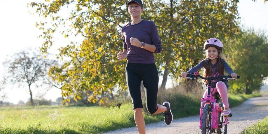 A mother jogging next to her daughter who is on her bike in the countryside.